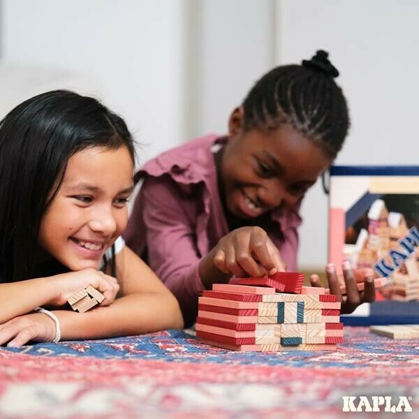 Zwei Kinder spielen mit Kapla-Bausteinen. Sie bauen ein Haus. Kapla-Logo unten rechts.