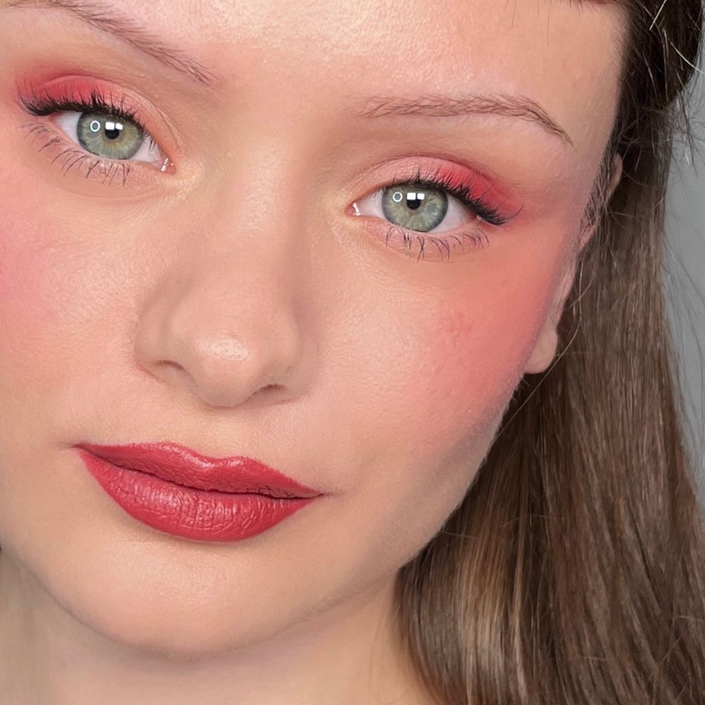 Nahaufnahme eines Gesichts mit Make-up. Roter Lidschatten, Rouge und Lippenstift. Grüne Augen.