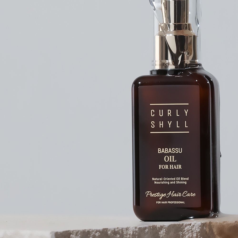 Braune Glasflasche mit goldfarbenem Sprühkopf. Aufschrift: CURLY SHYLL Babassu Oil for Hair. Prestige Hair Care.