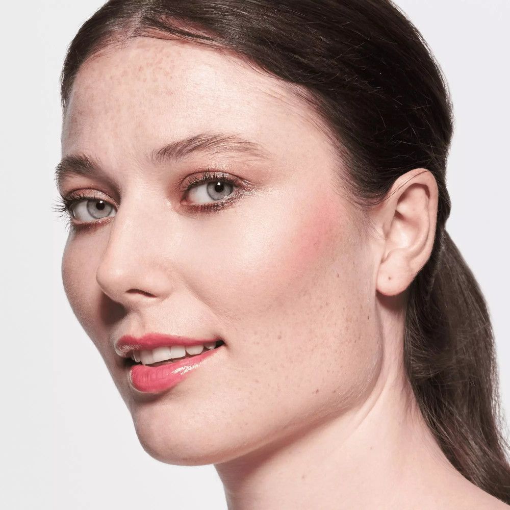 Porträt einer Frau mit rosafarbenen Lippen. Sie lächelt, trägt Make-up und hat Sommersprossen.