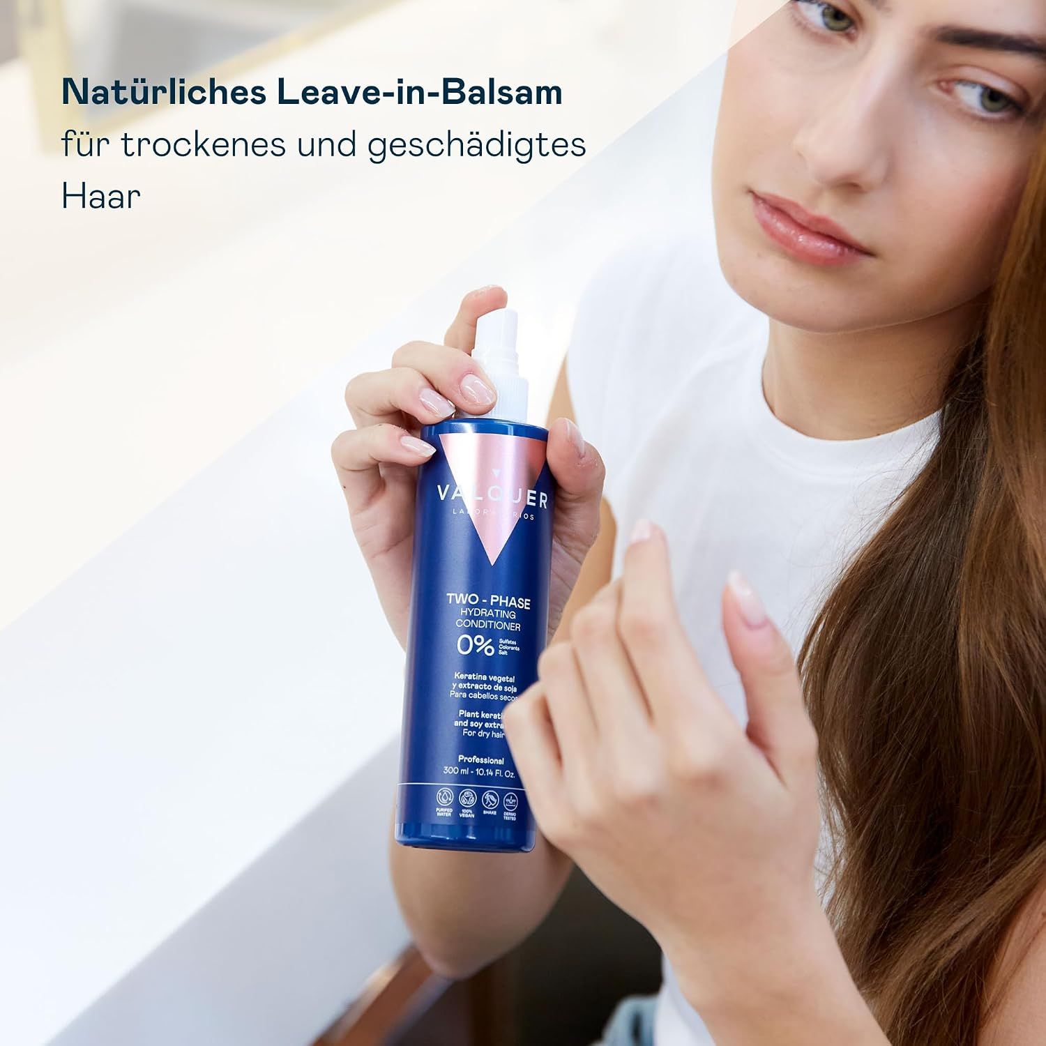 Frau hält eine blaue Sprühflasche mit der Aufschrift 'VALQUER TWO-PHASE HYDRATING CONDITIONER'.