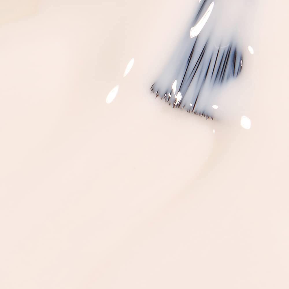 Pinsel in cremefarbenem Nagellack. Borsten zeigen nach unten. Flüssigkeit reflektiert Licht. Hintergrund ist cremefarben.