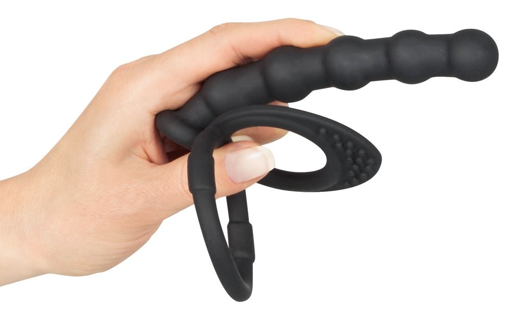Hand hält schwarzen Penis- und Hodenring mit Analdildo. Ring mit Noppen, Dildo mit geriffelter Oberfläche.