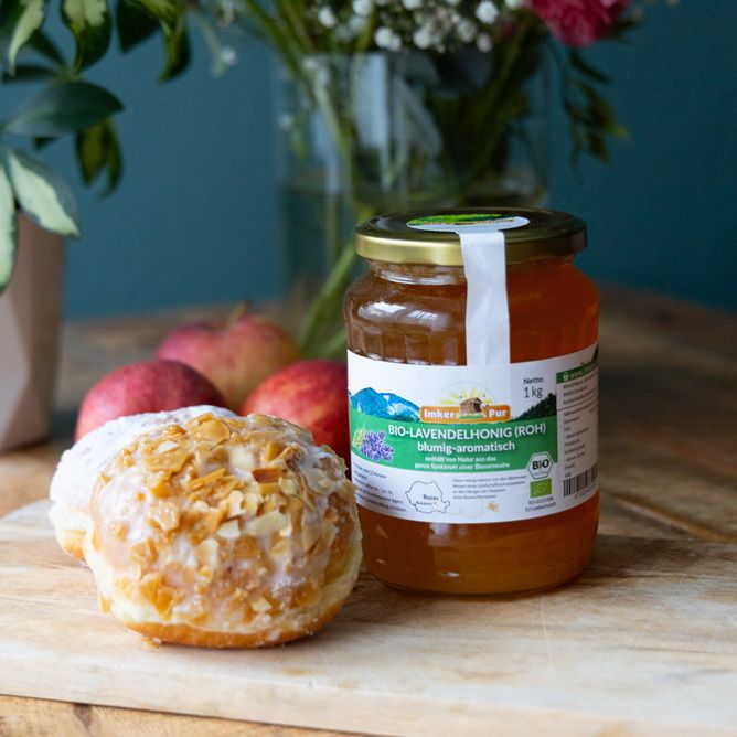 Glas Honig mit Etikett neben Gebäck und Äpfeln. Aufschrift: BIO-Lavendelhonig (roh).