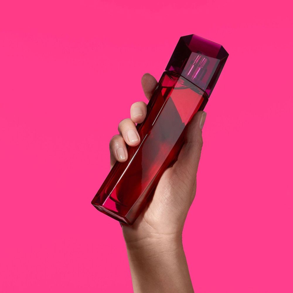 Hand hält einen rosa Flakon. Der Flakon hat einen kantigen Deckel. Hintergrund ist pink.