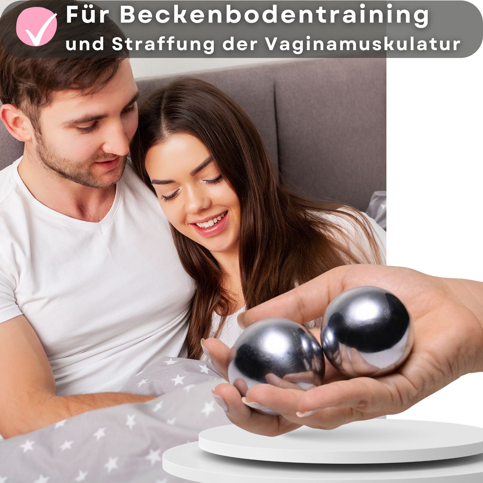 Zwei metallische Kugeln in einer Hand. Paar liegt auf einer Oberfläche. Hintergrund: Paar im Bett.
