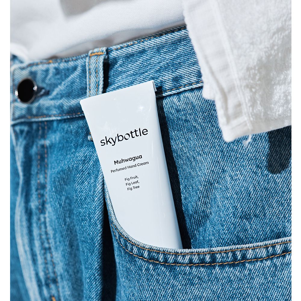 Weiße Tube in einer Jeans-Hosentasche. Aufschrift: skybottle, Muhwagua Perfumed Hand Cream. Text: Fig Fruit, Fig Leaf, Fig Tree.
