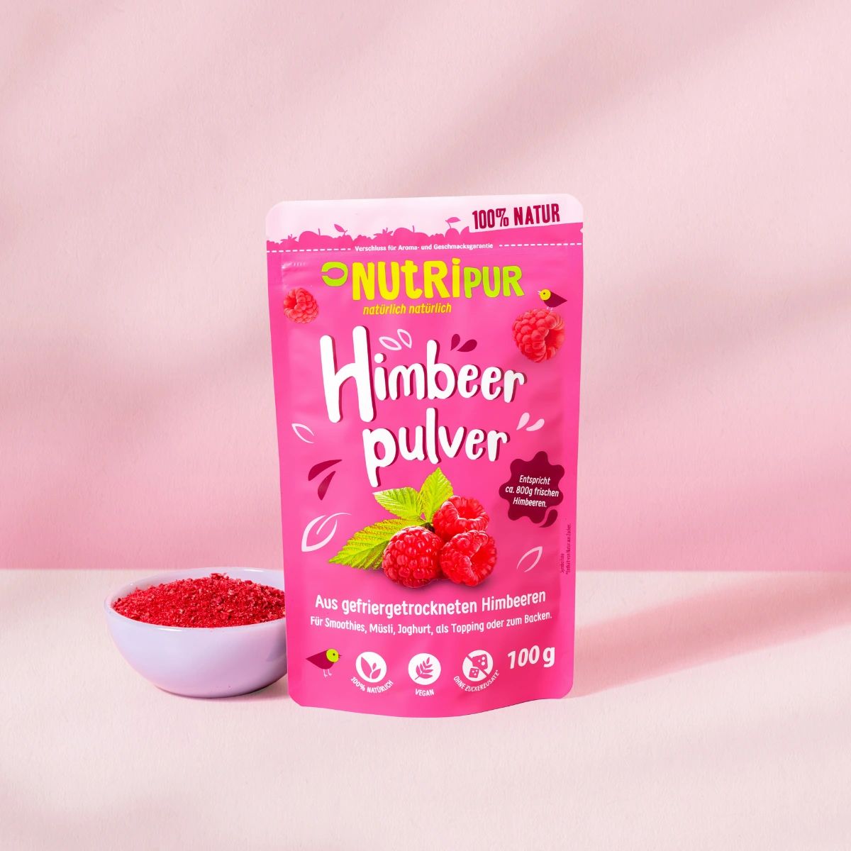 Rosa Beutel mit Himbeerpulver. Aufschrift: NutriPur, Himbeerpulver, 100% Natur. Eine Schale mit Pulver daneben.