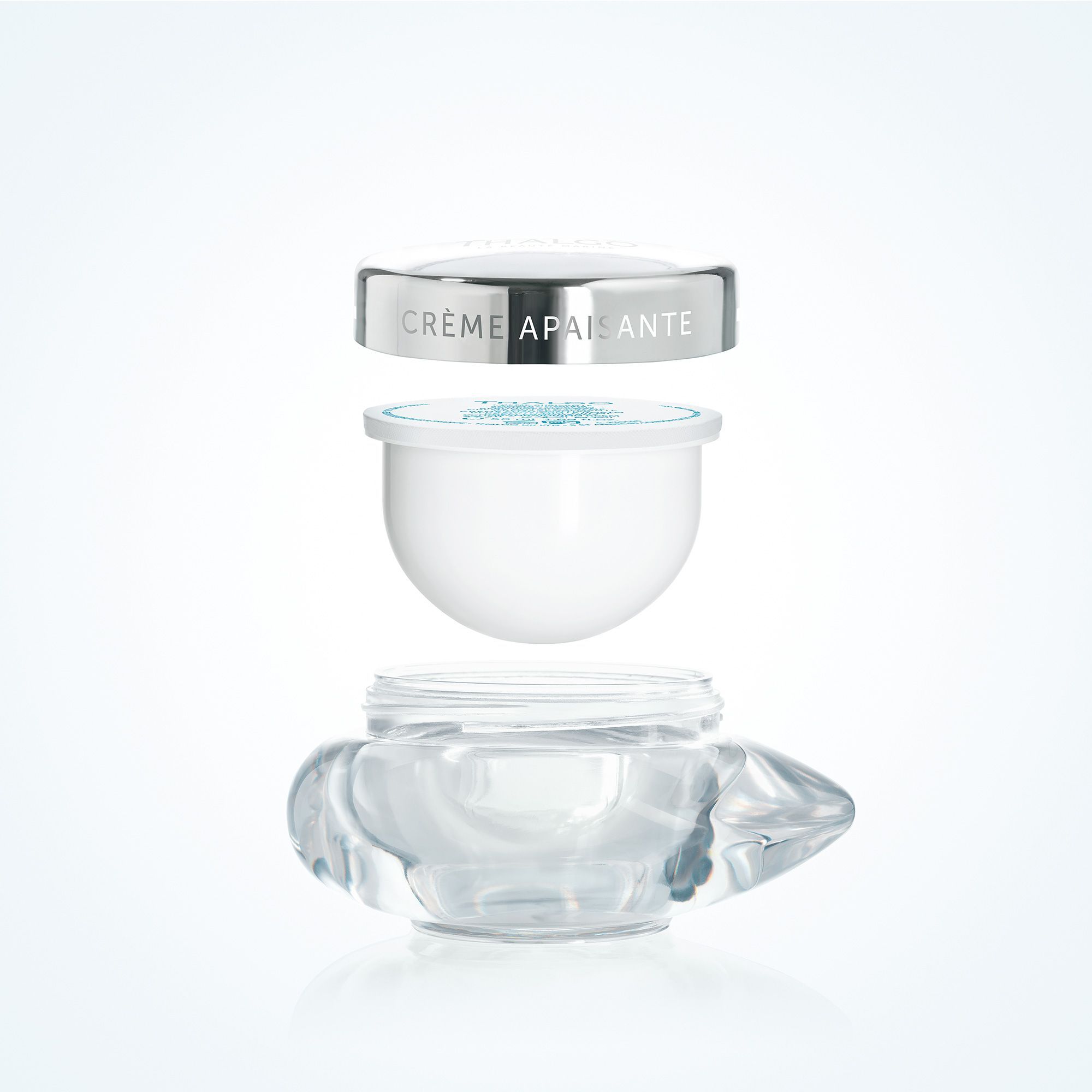 Drei Teile einer Creme-Verpackung: Deckel mit Schriftzug CRÈME APAISANTE, Nachfüllpackung und Glasbehälter. Weißer Deckel, transparente Basis.