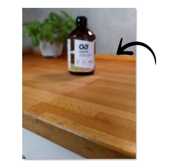 Braune Flasche OA wood oil auf einer Holzoberfläche. Pfeil zeigt auf die Flasche. Im Hintergrund eine Pflanze.