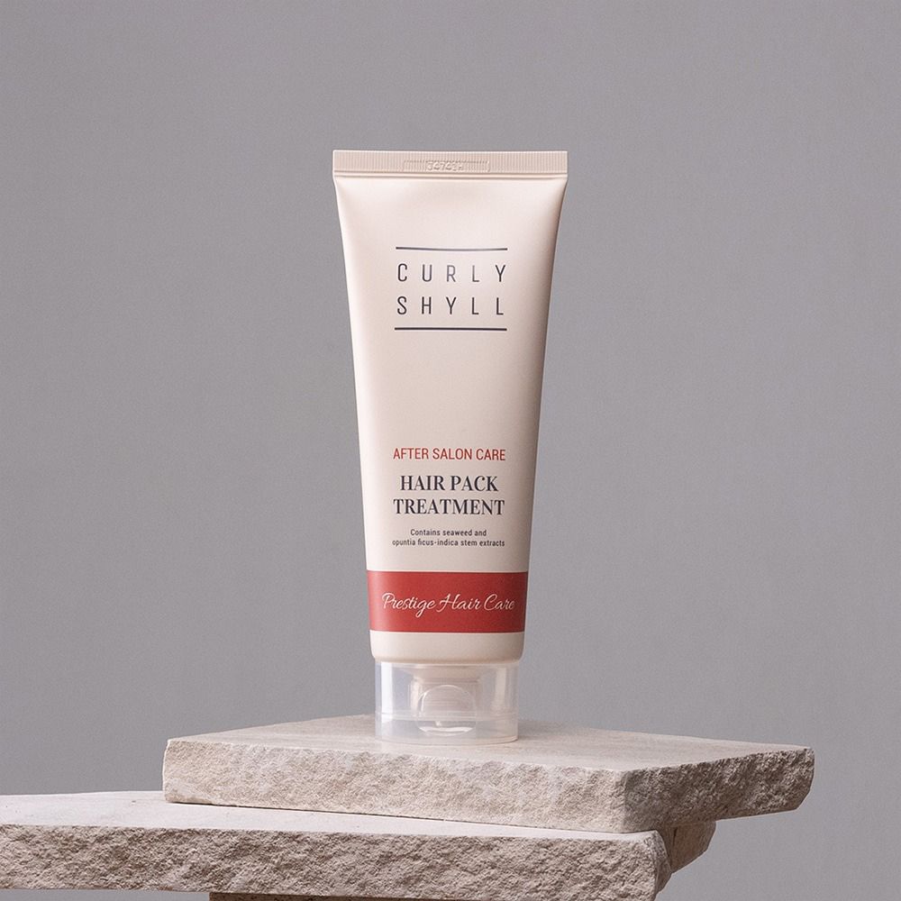 Beige Tube auf Stein. Aufschrift: CURLY SHYLL, After Salon Care, Hair Pack Treatment. Roter Streifen mit Text: Prestige Hair Care.