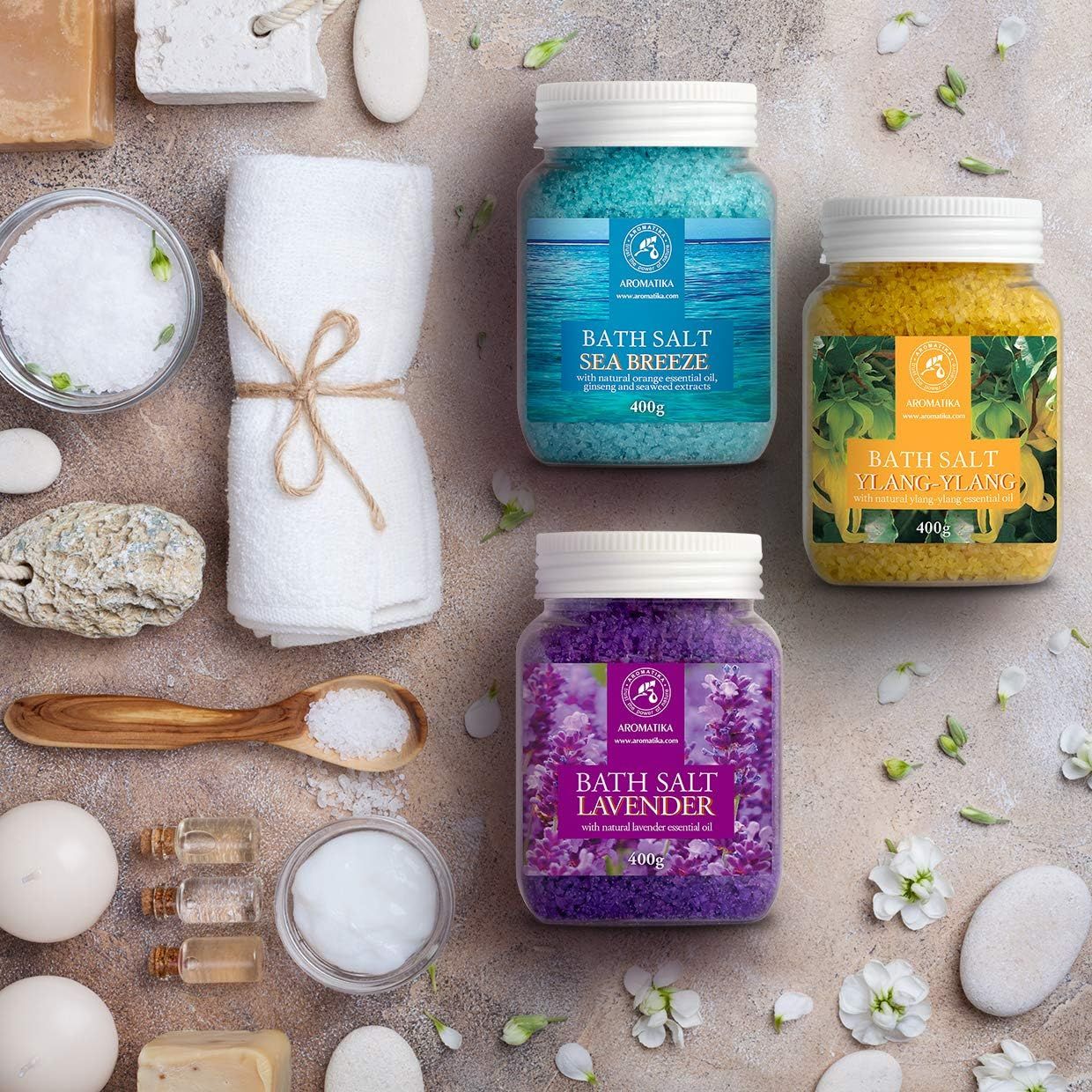 Drei Gläser Badesalz und Zubehör. Gelb, blau und lila. Etiketten mit Produktnamen und Logo. Gelb: Ylang-Ylang. Blau: Meeresbrise. Lila: Lavendel. Zusätzliche Produkte.