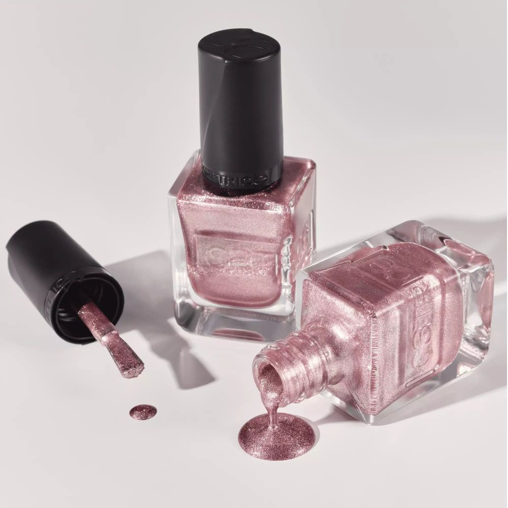 Drei Nagellackflaschen. Eine mit Pinsel, eine umgekippt, eine aufrecht. Der Lack ist rosa-metallic.