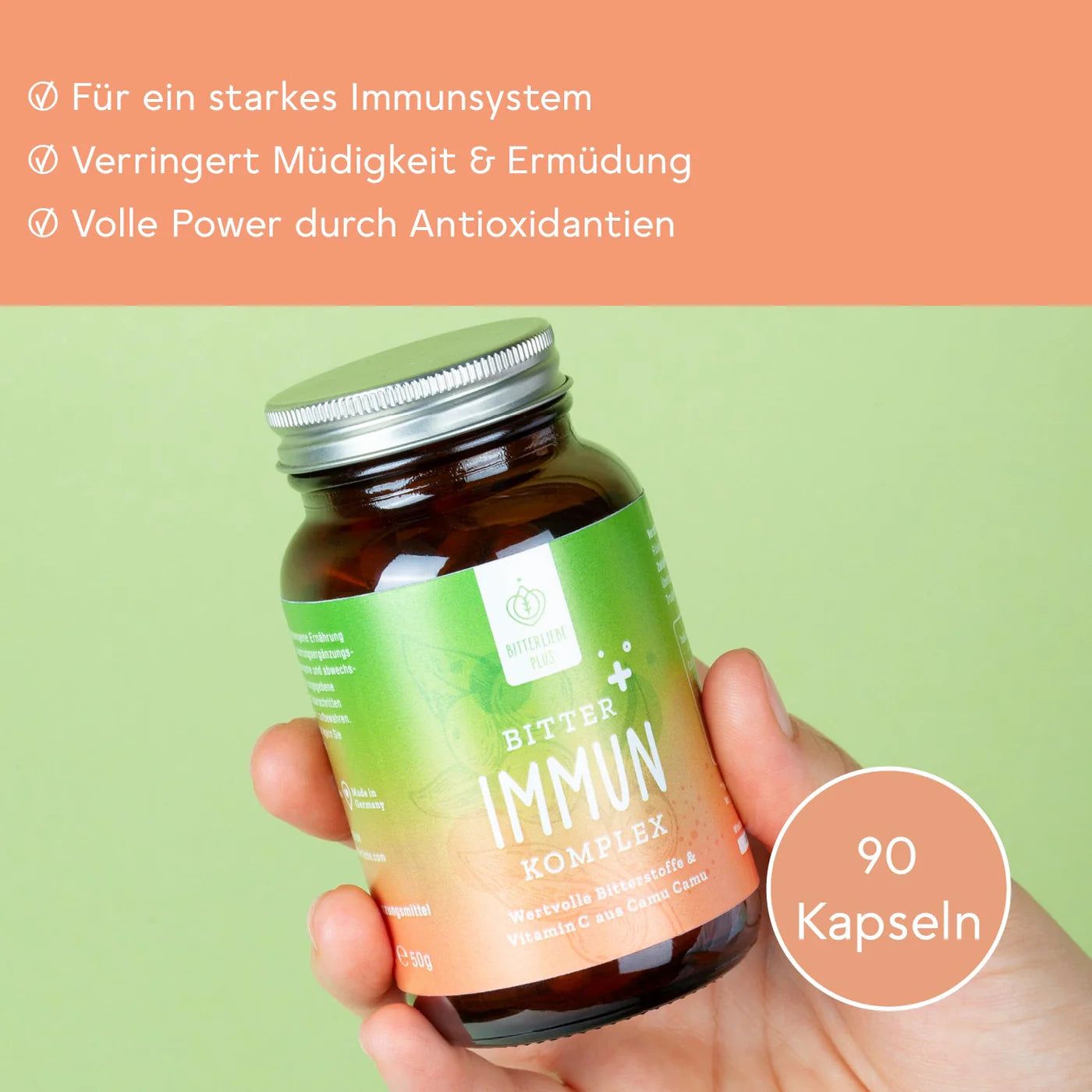 Hand hält eine braune Flasche BitterLiebe Immun Komplex. Orangefarbener Hintergrund mit Text. 90 Kapseln.