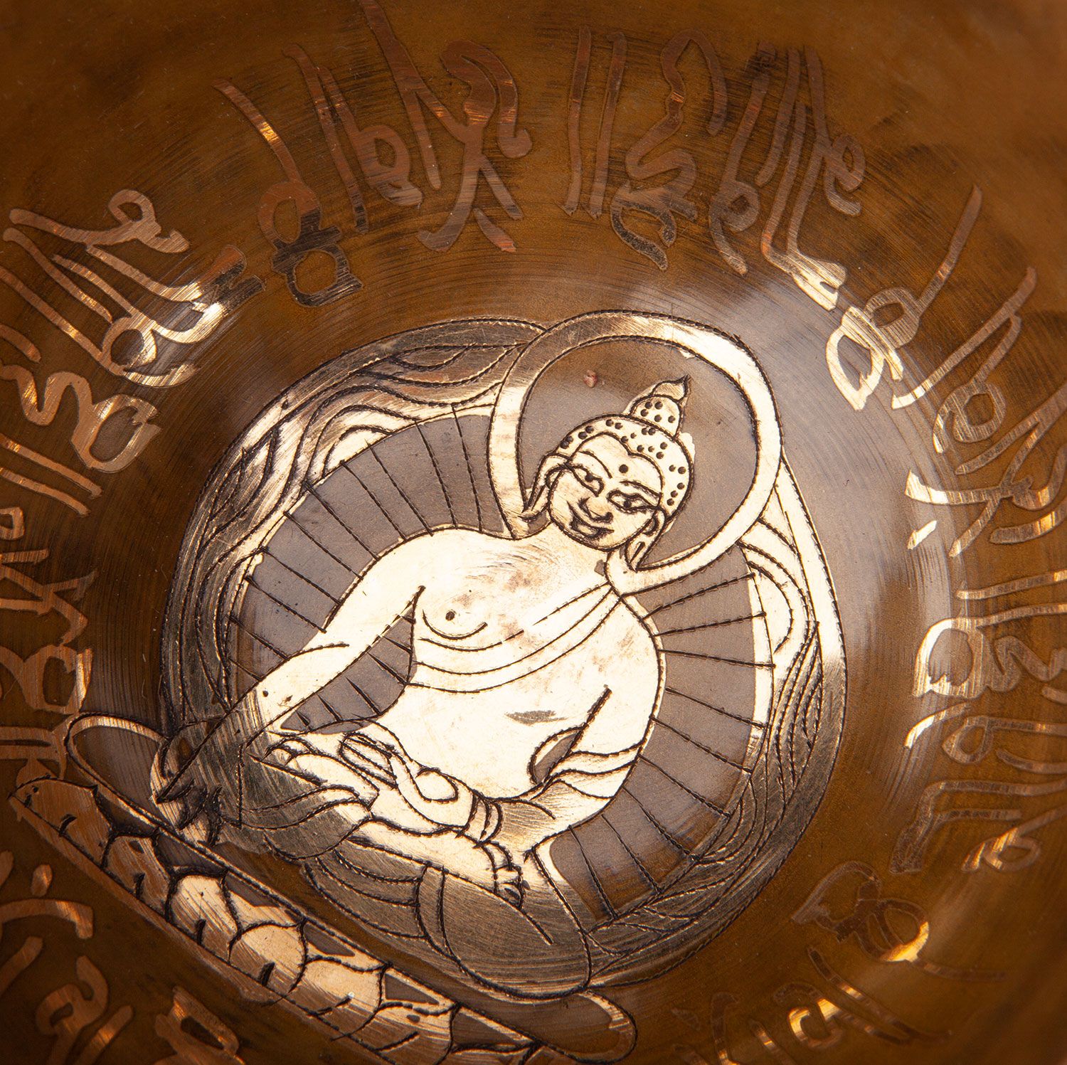 Nahaufnahme des Inneren einer bronzefarbenen Klangschale. Ein Buddha-Motiv ist sichtbar. Die Schale hat Gravuren.