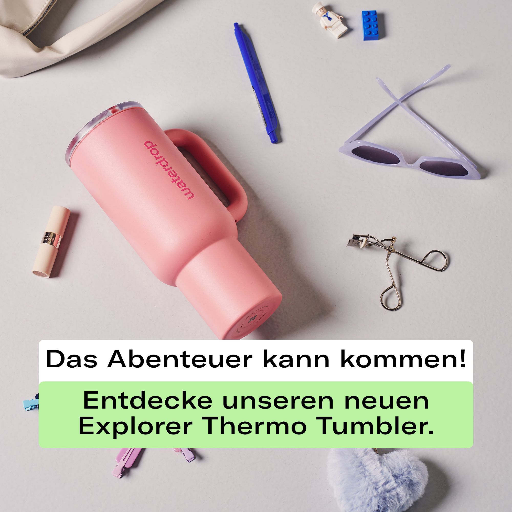 Soft Pink Thermobecher XL mit Henkel, umgeben von Alltagsgegenständen.