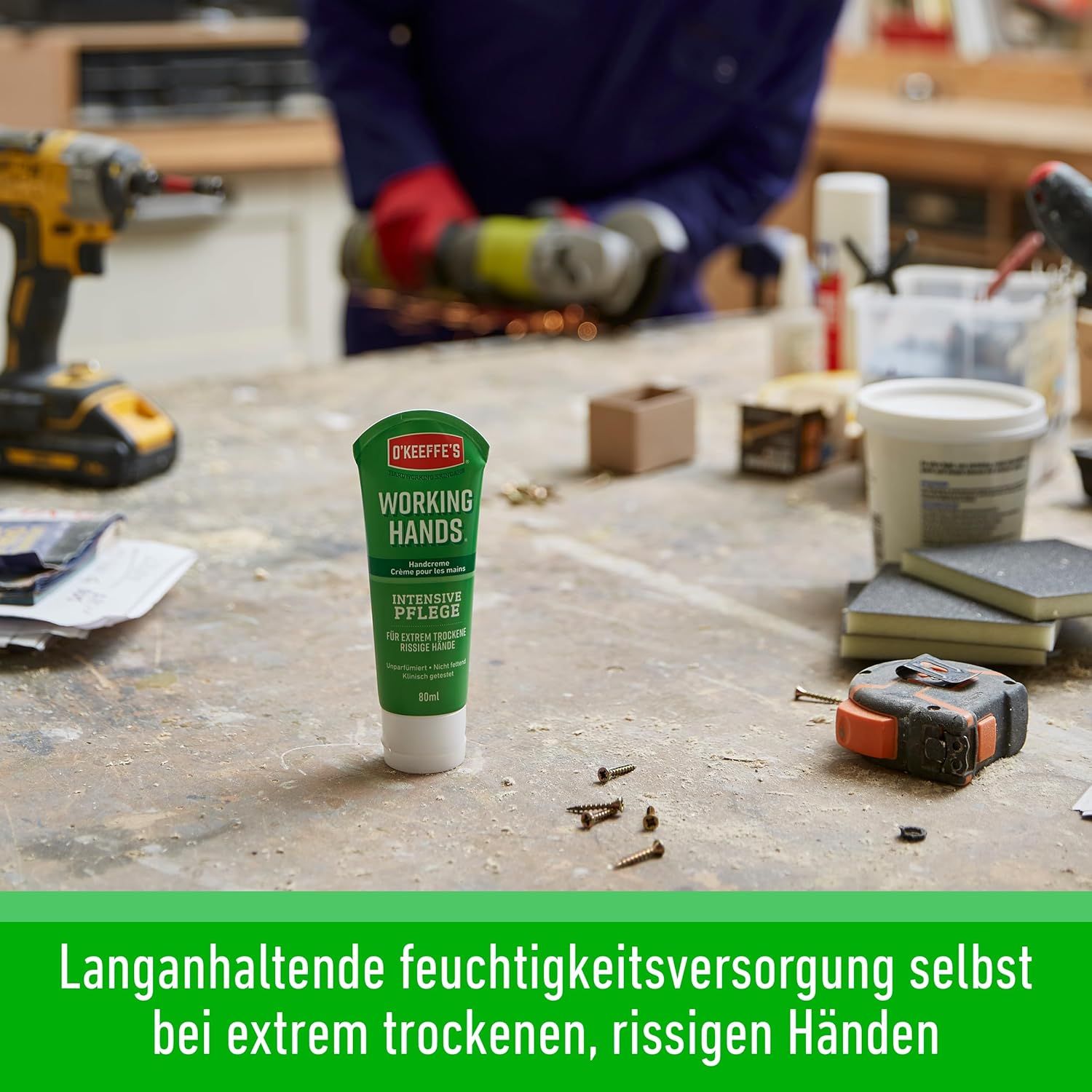 O'Keeffe's Working Hands Tube auf einer Werkbank. Werkzeuge im Hintergrund. Text: Langanhaltende Feuchtigkeitsversorgung bei extrem trockenen Händen.