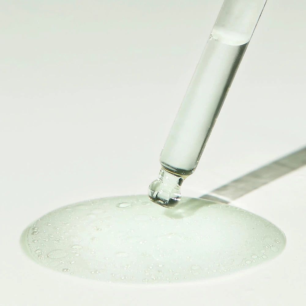 Pipette mit Serum auf einer Oberfläche. Serum bildet einen Fleck. Keine Flasche sichtbar.