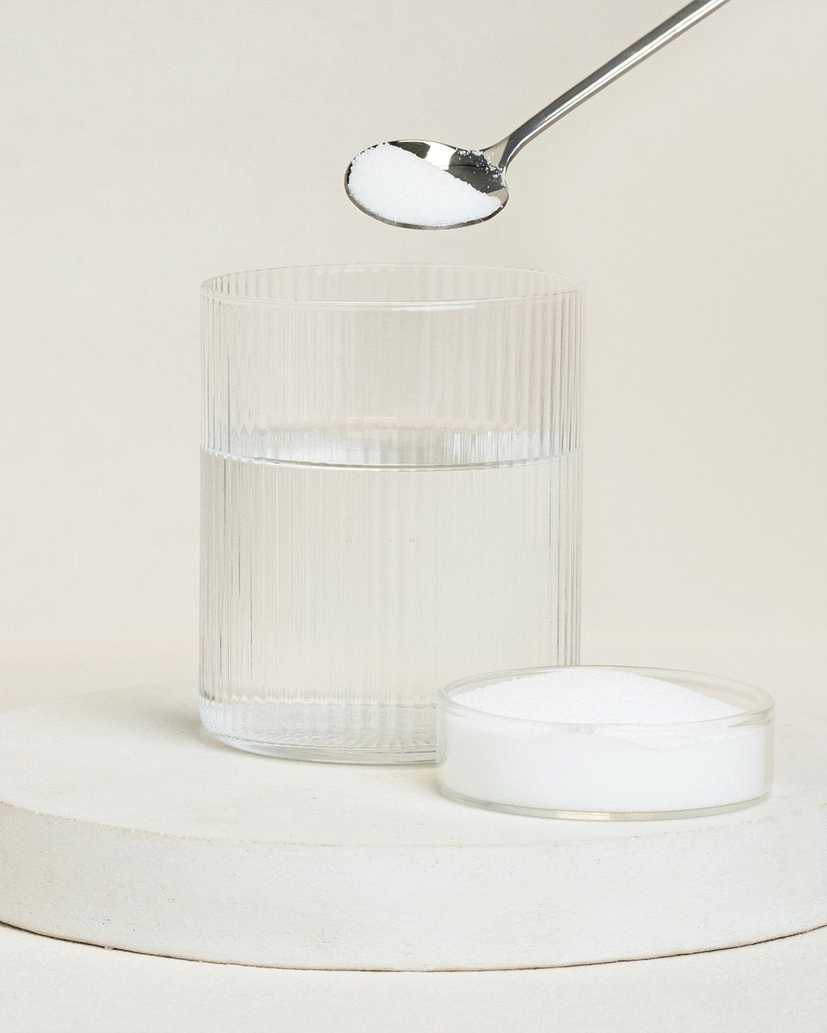 Feines weißes Pulver auf einem Löffel über einem Glas Wasser. Daneben eine kleine Schale mit Pulver.