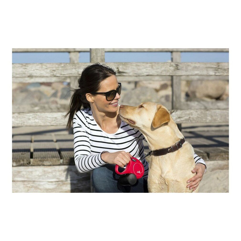 Frau mit Sonnenbrille und Hund. Sie hält eine rote Hunderolle. Hund leckt sie.