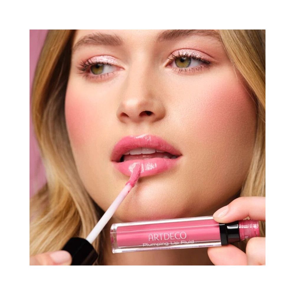 Frau trägt Artdeco Lipgloss Plumping Fluid 35 Juicy Berry auf. Rosa Lippen, Applikator im Mund.