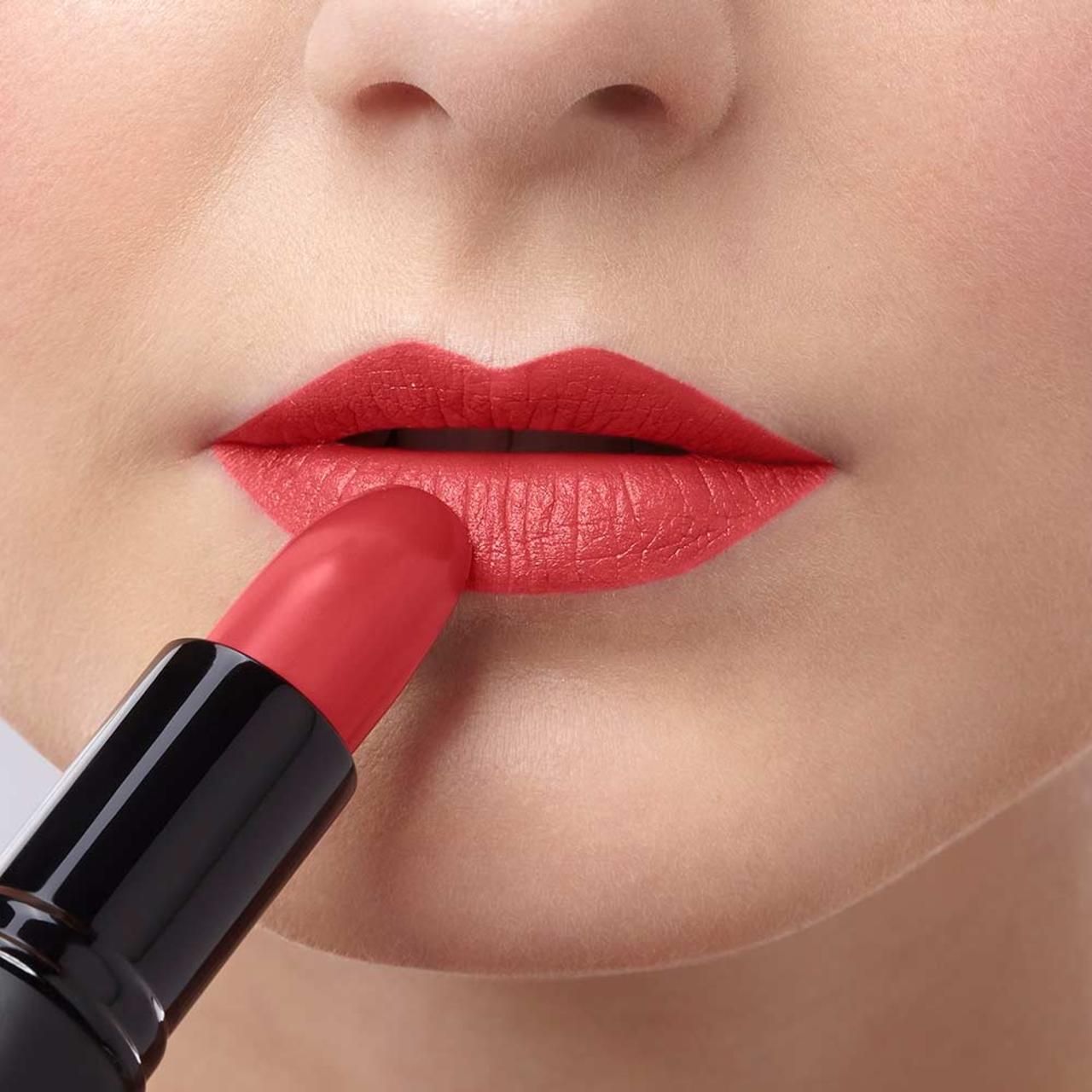 Person trägt roten Lippenstift auf den Lippen auf. Lippenstift in schwarzer Hülse.