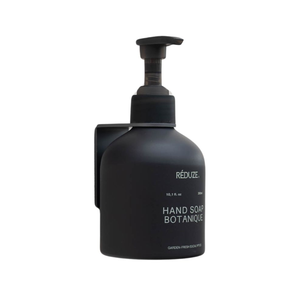 Schwarze Handseife mit Wandhalterung. Aufschrift: HAND SOAP BOTANIQUE. Schwarzer Spender mit Pumpkopf. Wandhalterung aus Metall.
