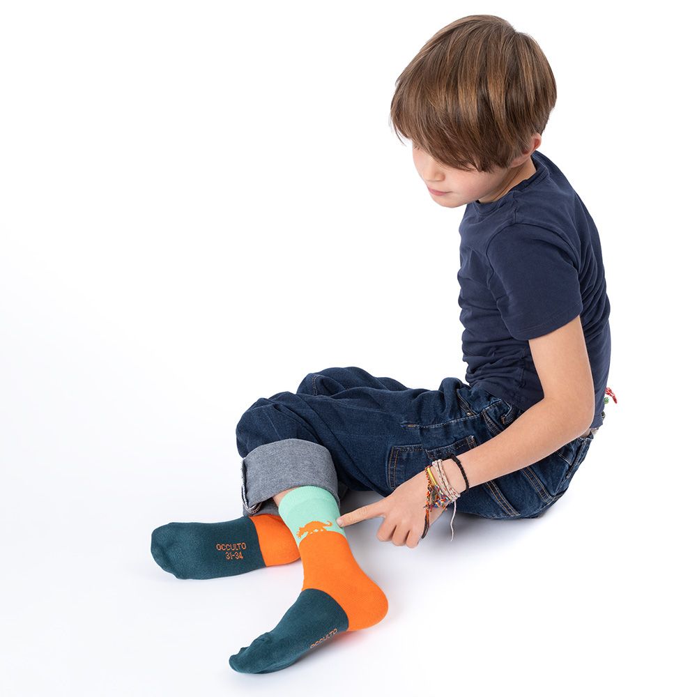 Kind sitzt und zeigt auf eine Socke. Socke mit grünem und orangefarbenem Design. Blaue Jeans.