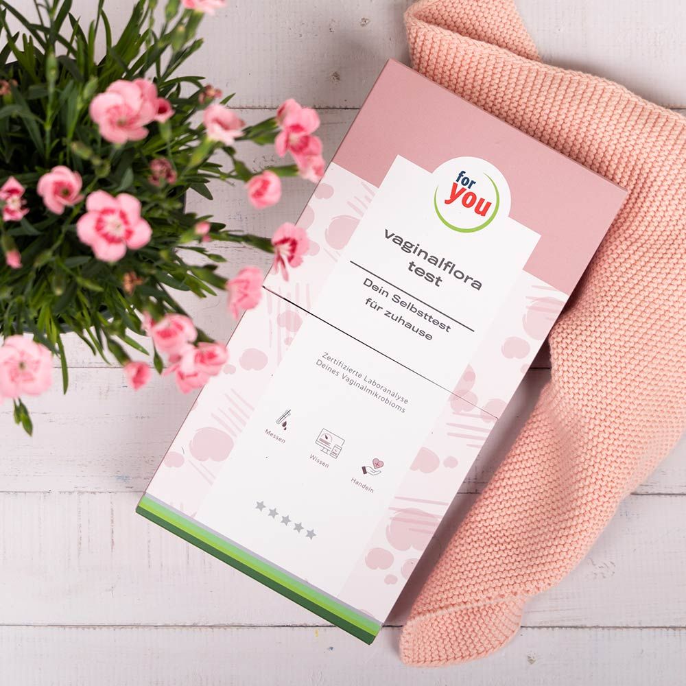 Rosa Verpackung mit Aufschrift "for you vaginalflora test". Auf einem rosa Stoff und neben Blumen.