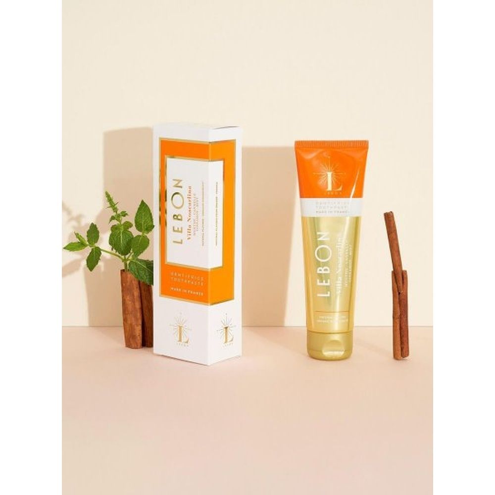 Zahnpasta-Tube LEBON Villa Noacarlina neben Verpackung und Zimtstange. Orange-gelbe Tube, weiße Verpackung mit Logo.