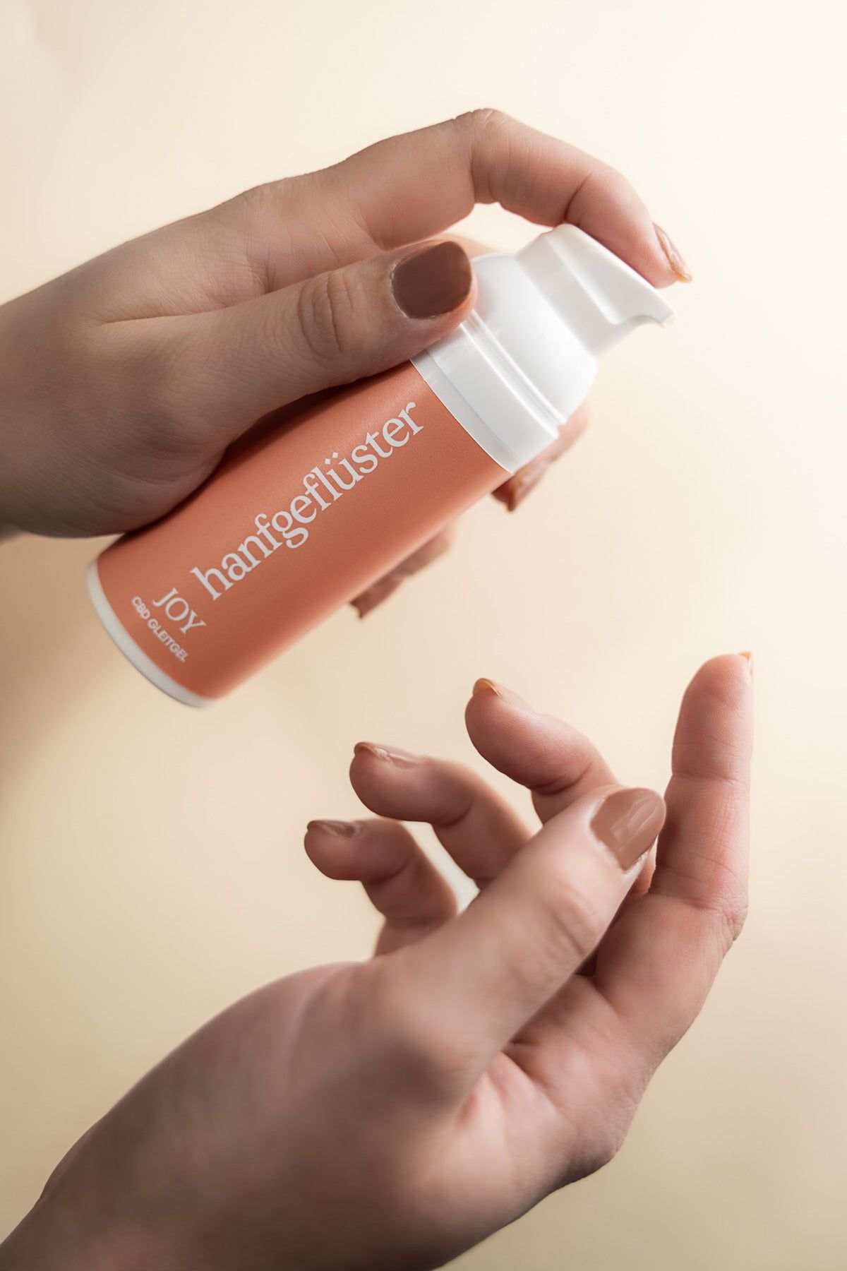 Hände halten eine orangefarbene Flasche mit weißer Schrift. Aufschrift: hanfgeflüster JOY CBD Gleitgel.