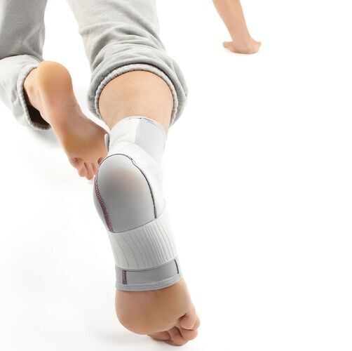 Knöchelbandage, grau-weiß. Bandage am Fuß getragen. Klettverschlüsse und Verstärkungen sichtbar.