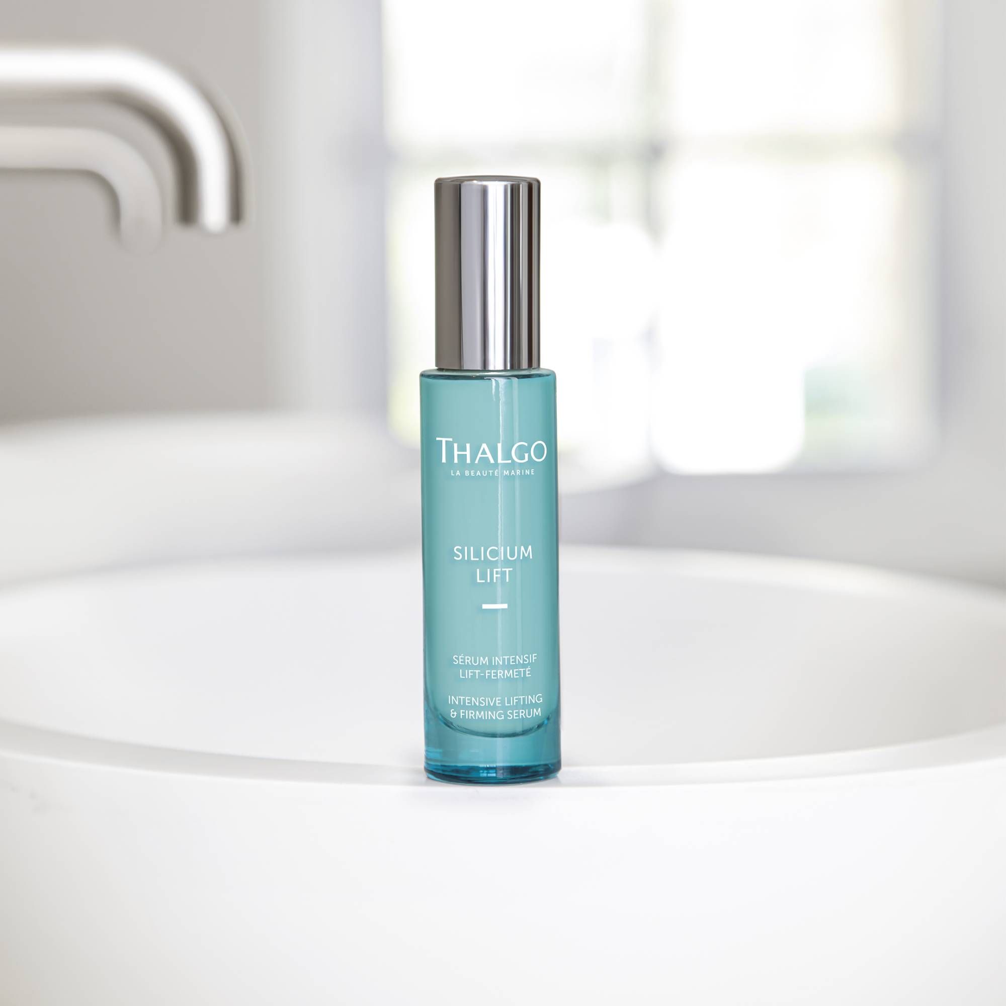 Türkisgrüne Flasche mit silbernem Deckel auf weißem Waschbecken. Beschriftung: THALGO, SILICIUM LIFT, INTENSIVE LIFTING & FIRMING SERUM.