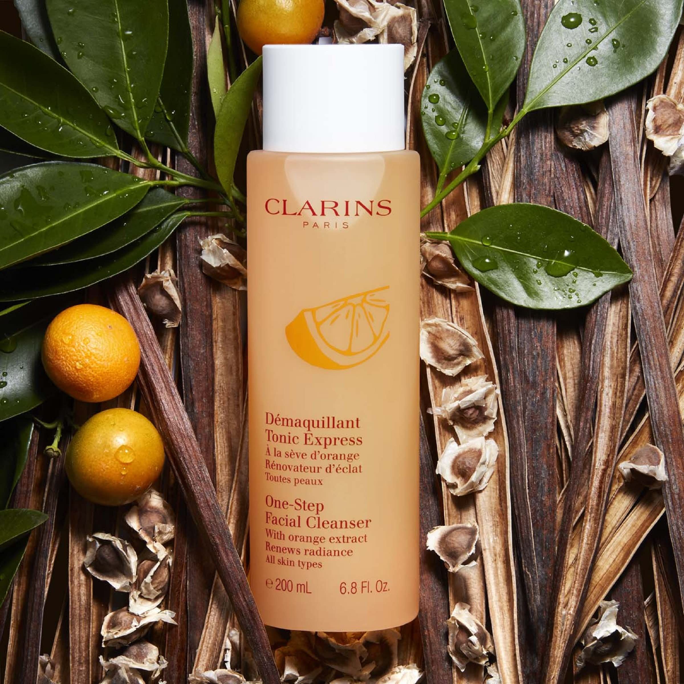 Orangefarbene Flasche mit weißem Deckel, umgeben von Blättern und Orangen. Aufschrift: Clarins Paris, D
emaquillant Tonic Express.