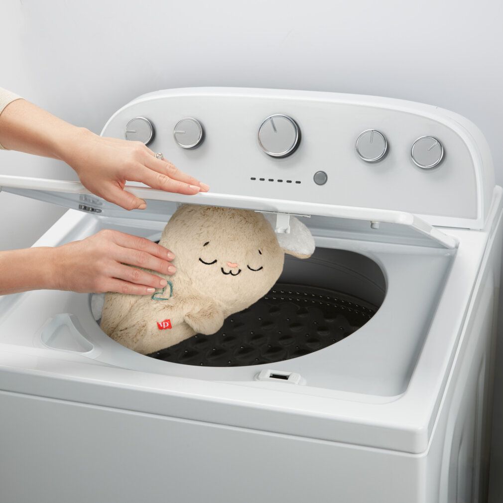 Beiges Schlummer-Häschen wird in eine Waschmaschine gelegt. Waschmaschinentür ist offen.