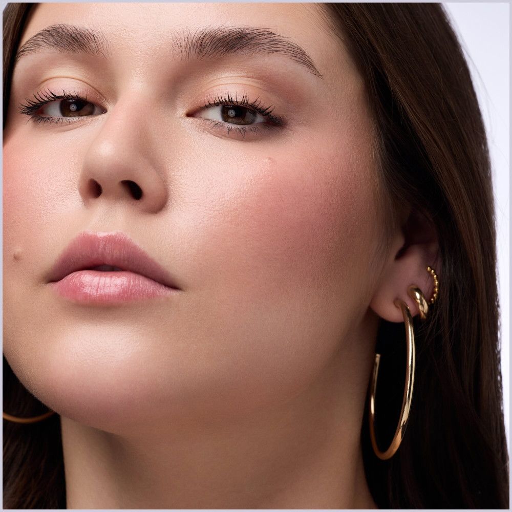 Nahaufnahme einer Frau mit Make-up. Rouge auf den Wangen. Goldene Ohrringe.