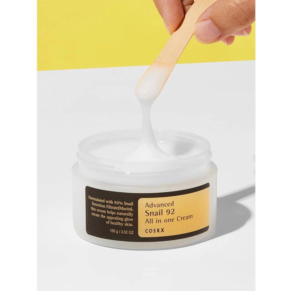 COSRX All in One Cream Tiegel mit Spatel, der eine weiße Creme entnimmt.