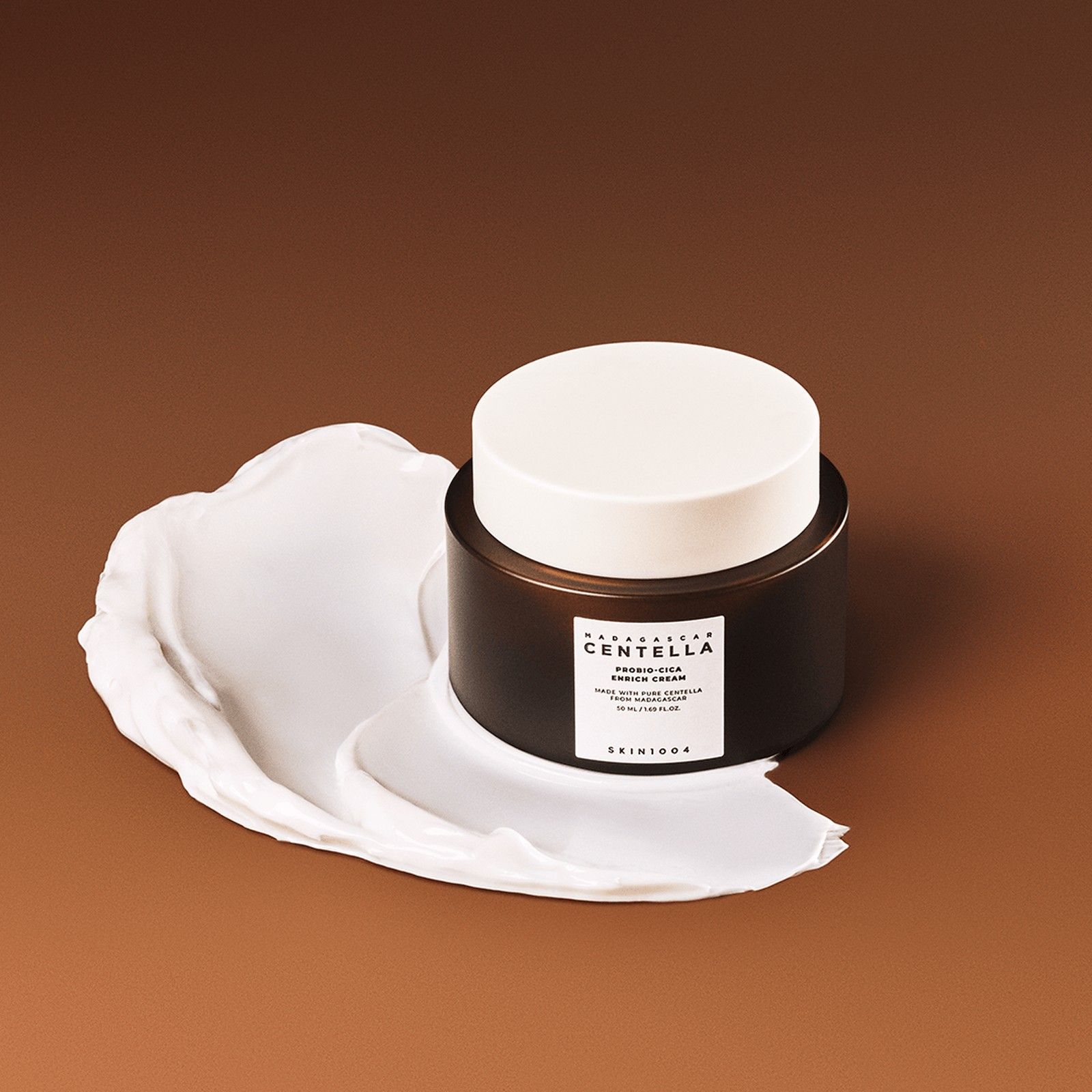 SKIN1004 Madagascar Centella Probio-Cica Enrich Cream mit einer Creme-Spur auf braunem Hintergrund.