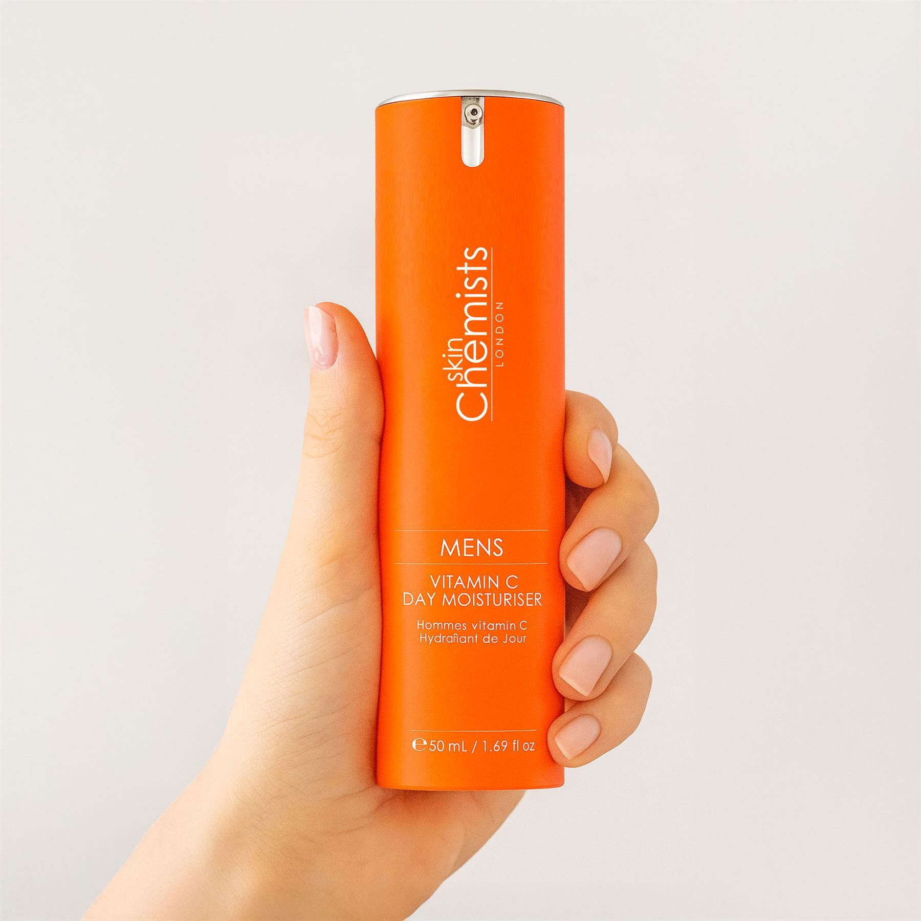 Eine Hand hält eine orangefarbene Flasche SkinChemists Vitamin C Tages-Feuchtigkeitscreme für Männer.