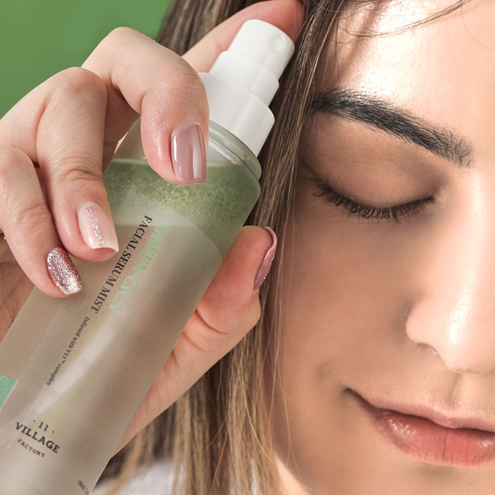 Person sprüht Serum auf ihr Gesicht. Flasche mit grünem Streifen und weißem Deckel. Beschriftung: Green Cica Facial Serum Mist.
