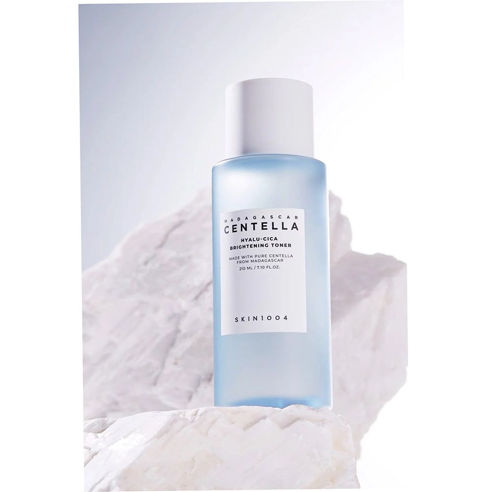 Blaue Flasche mit weißem Deckel auf einem weißen Stein. Aufkleber mit Text: CENTELLA, HYALU-CICA, BRIGHTENING TONER. Marke: SKIN1004.
