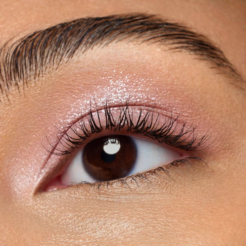 Nahaufnahme eines Auges mit rosafarbenem Lidschatten. Lange Wimpern. Braune Iris.