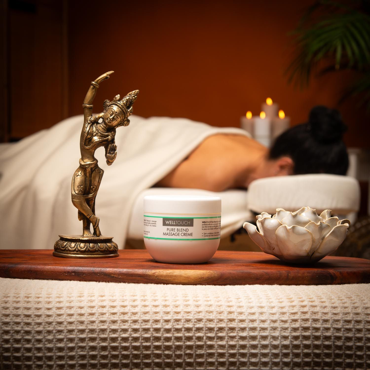 Weißes Creme-Gefäß mit grüner Beschriftung. Aufschrift: Welltouch Pure Blend Massage Creme. Vor Massage-Szene.