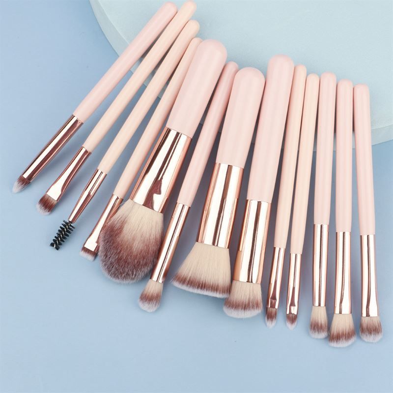 Make-up Pinsel-Set. Rosa Griffe, goldfarbene Metallhülsen, verschiedene Pinselköpfe. Auf blauem Untergrund.