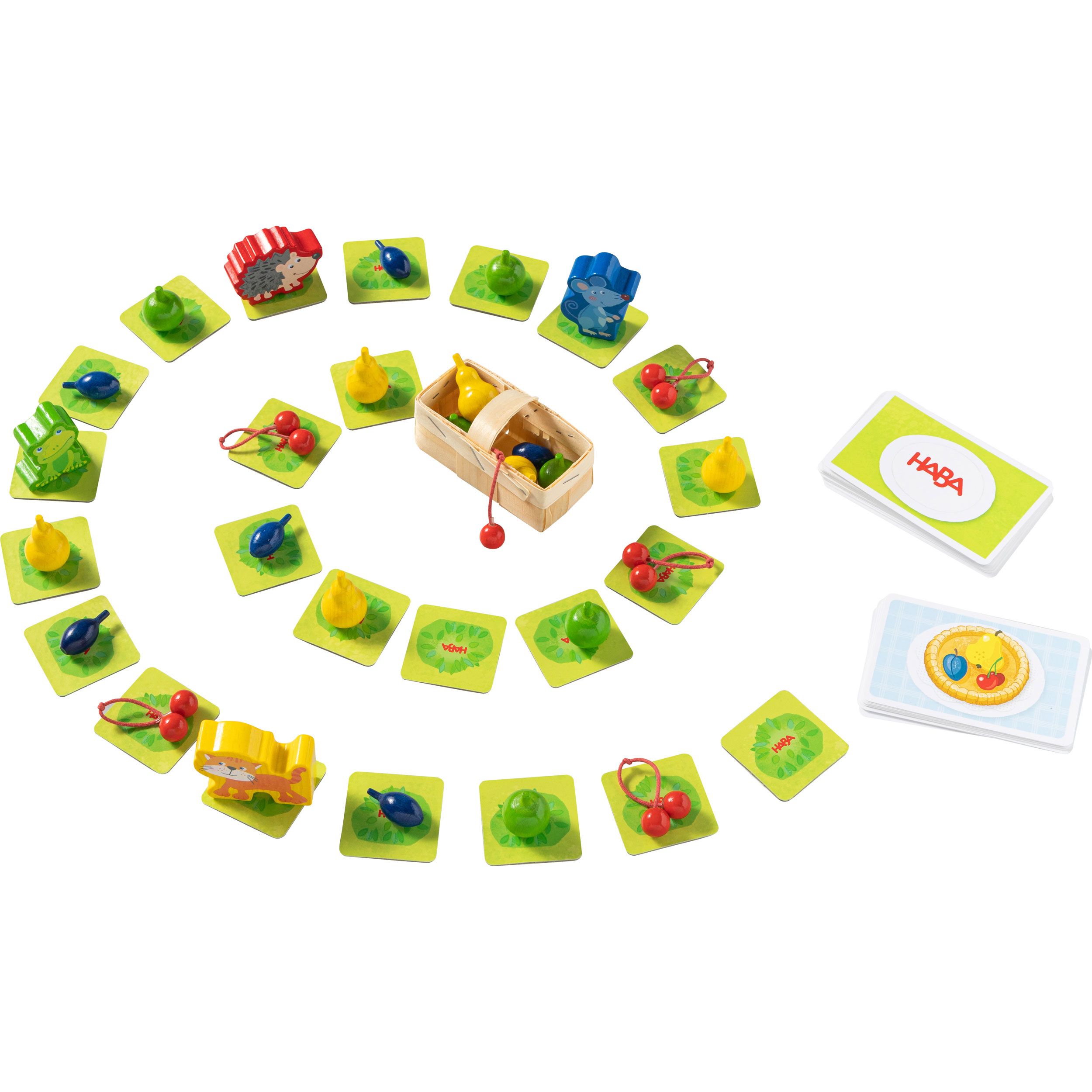 Spielmaterialien, darunter Spielkarten, Holzfiguren, Obstkörbe und Spielsteine. Auf grünem Untergrund angeordnet.