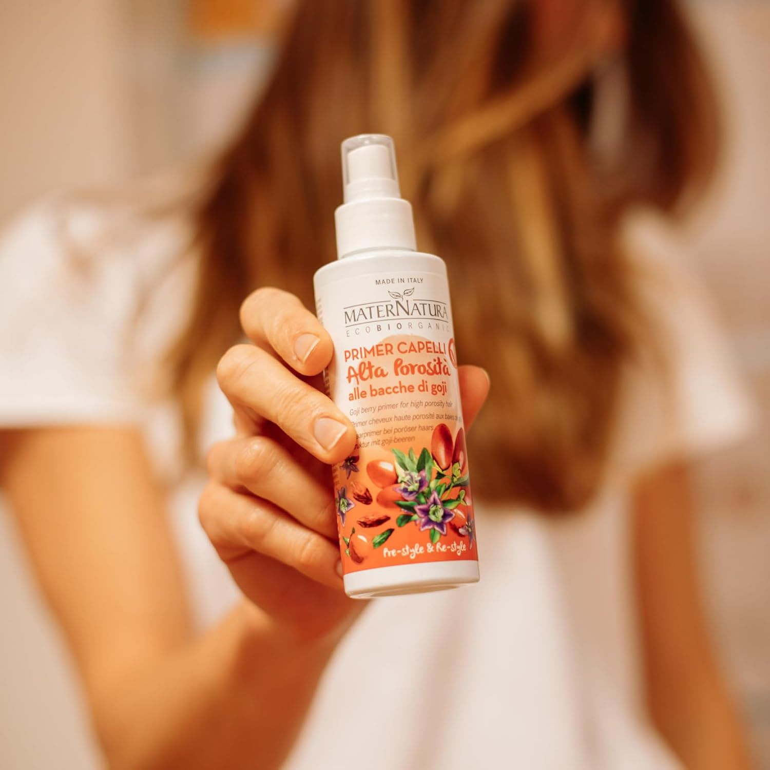 Maternatura Haar Primer mit Goji-Beeren. Weißer Sprühflakon mit orangefarbenem Etikett, gehalten von einer Hand.