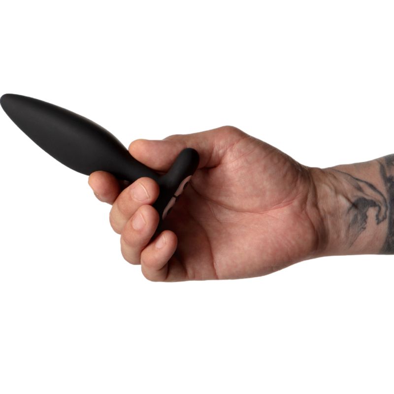 Hand hält schwarzes, anales Stimulationsgerät. Längliche Form, T-förmiger Griff.