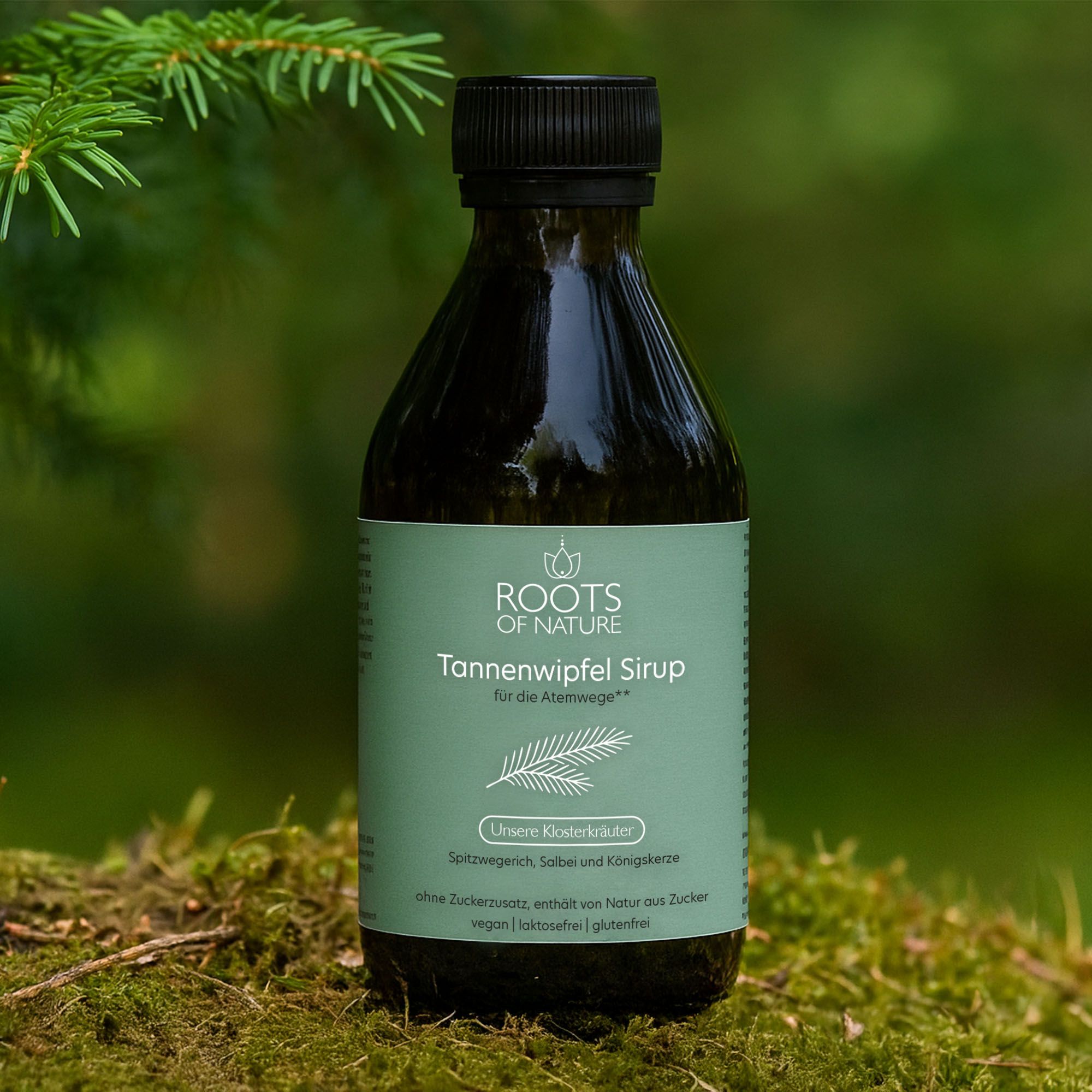 Braune Glasflasche ROOTS OF NATURE Tannensirup. Aufschrift: Tannensirup für die Atemwege. Steht auf Moos. Schwarzer Deckel.