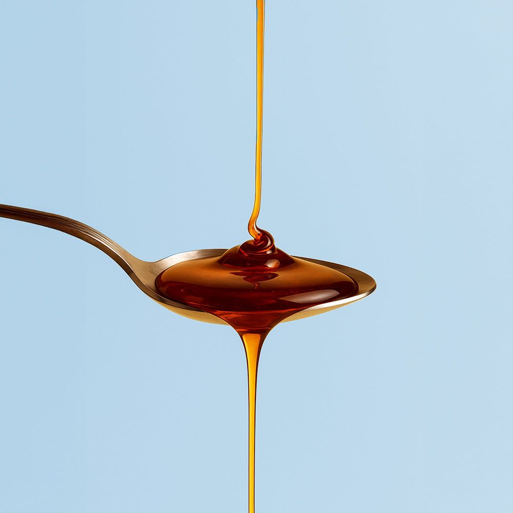 Löffel mit brauner Flüssigkeit. Flüssigkeit tropft vom Löffel. Blauer Hintergrund.