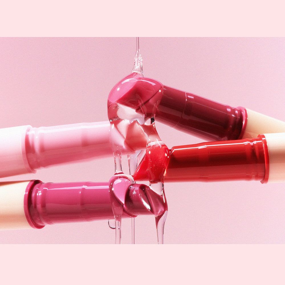 Mehrere Lippenstifte, aus denen eine transparente Flüssigkeit fließt. Die Lippenstifte sind in verschiedenen Rosatönen.